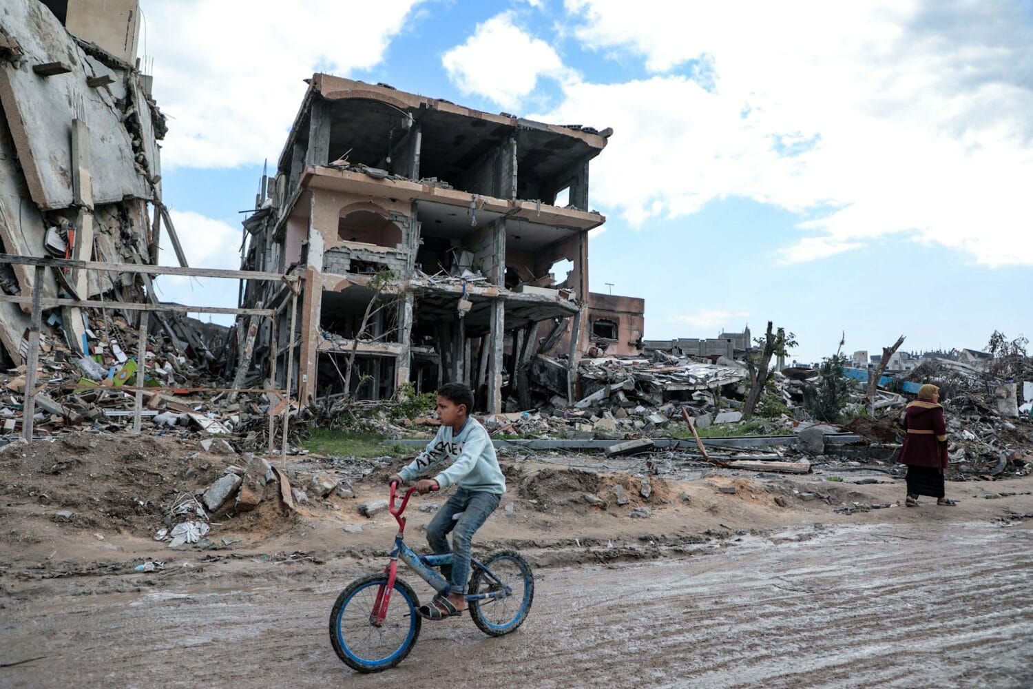 Boy rides a bicycle through a war-torn area.