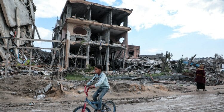 Boy rides a bicycle through a war-torn area.
