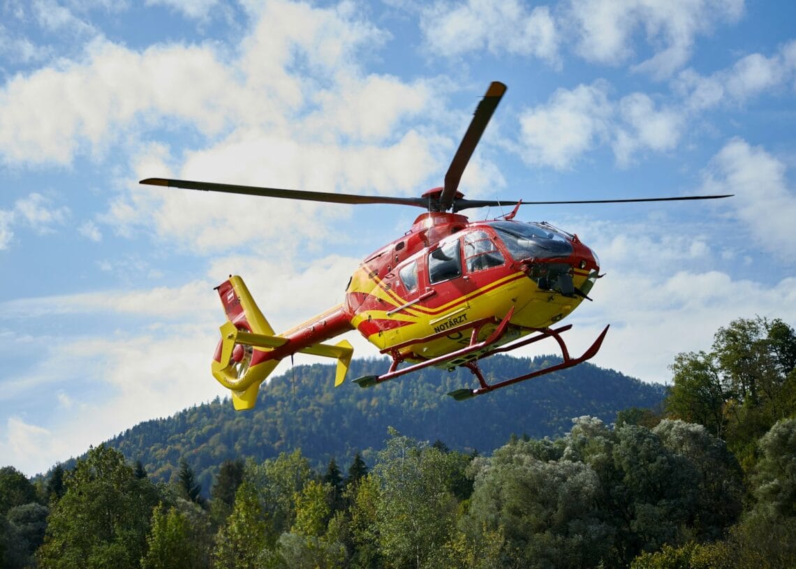 red and yellow helicopter flying over green trees during daytime