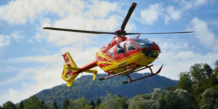 red and yellow helicopter flying over green trees during daytime