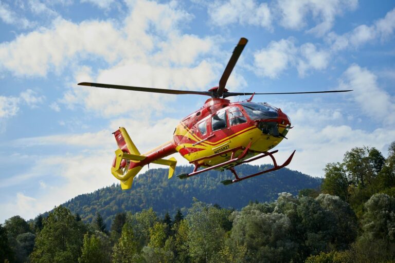 red and yellow helicopter flying over green trees during daytime