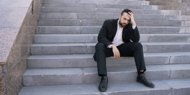 Man in suit sitting on outdoor stairs looking down.