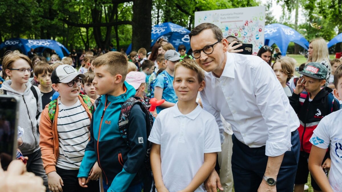 Mateusz Morawiecki, wówczas premier, pozuje z dziećmi podczas wydarzenia programu 800+ na zielonym terenie