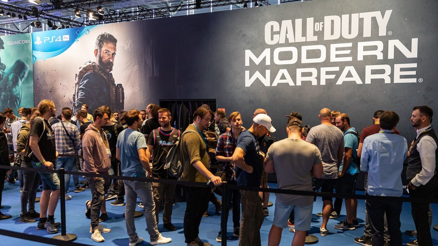 Kolejka graczy przy stoisku Call of Duty: Modern Warfare na targach Gamescom, za nimi duży baner z logo gry i postacią.