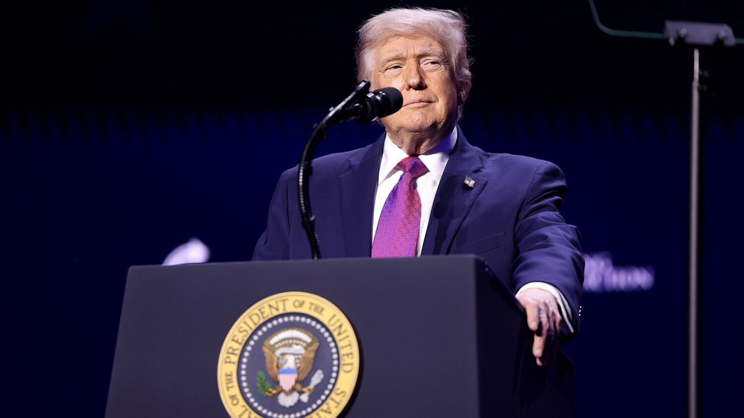 Donald Trump przemawia do publiczności za mównicą z pieczęcią prezydenta USA podczas wiecu w Arizonie.