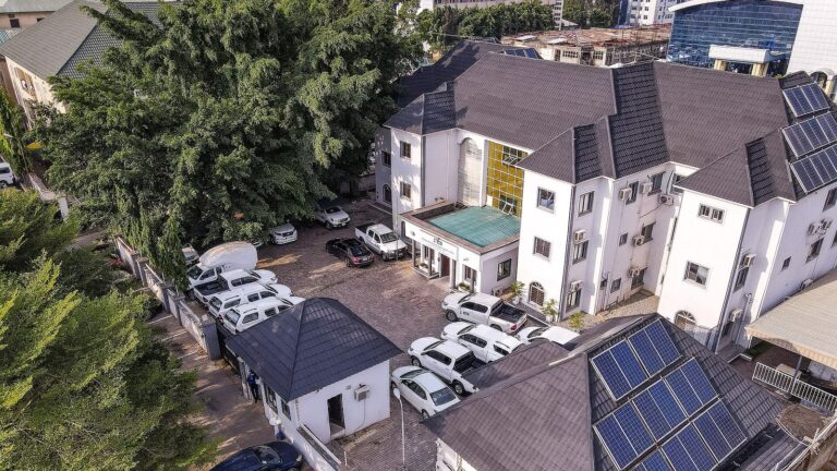 Budynek centrali Nigeryjskiego Centrum Kontroli Chorób (NCDC) z zaparkowanymi samochodami i panelami słonecznymi na dachu.
