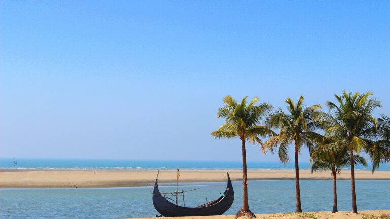Plaża w Inani koło Cox's Bazar w Bangladeszu: drewniana łódź na piasku i palmy nad zatoką.