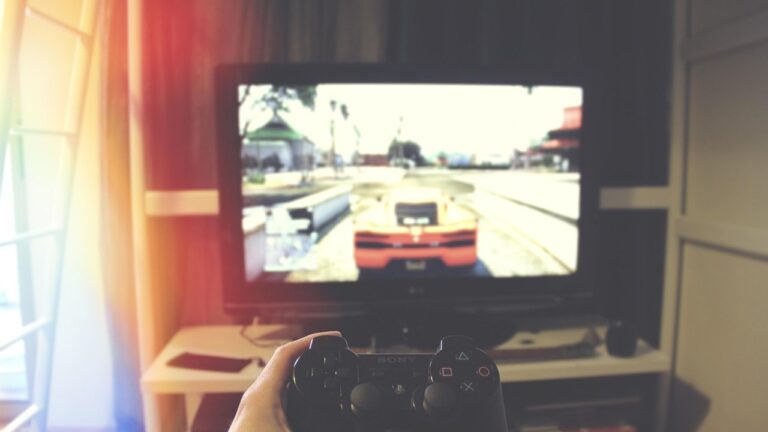 Pad PlayStation w dłoni przed telewizorem, na ekranie gra samochodowa w mieście