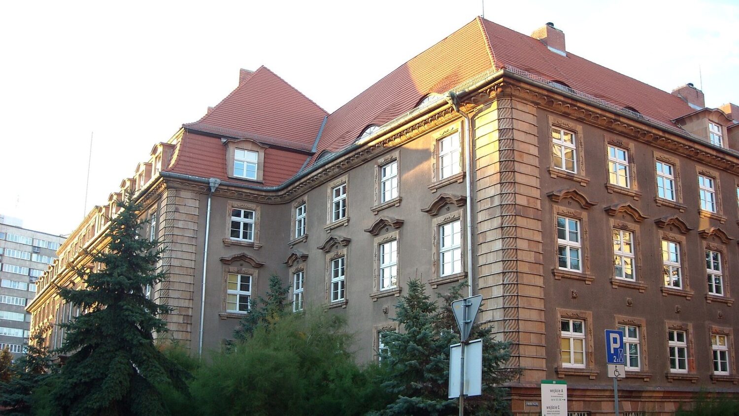 Ceglany gmach ZUS przy ulicy Pretficza we Wrocławiu, z czerwonym dachem i zielenią przed budynkiem.