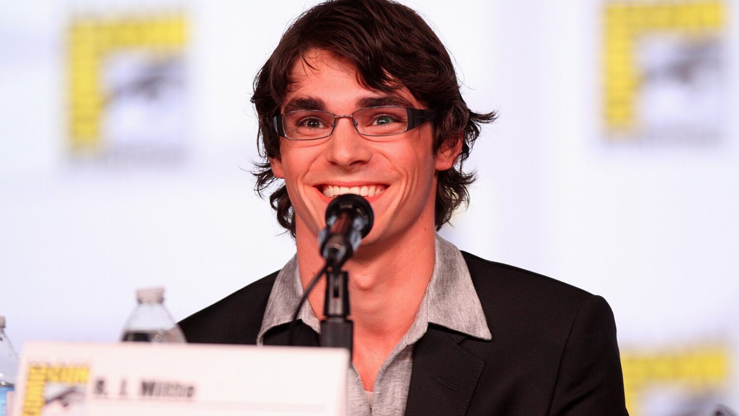 Aktor RJ Mitte, uśmiechnięty, przy mikrofonie podczas panelu na Comic-Con w San Diego w 2012 roku.