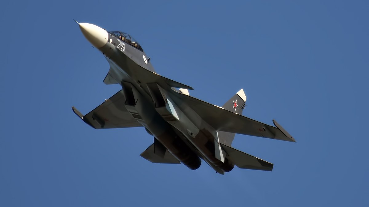 Rosyjski myśliwiec Su-30SM Marynarki Wojennej w locie na tle błękitnego nieba, widoczna czerwona gwiazda na ogonie.