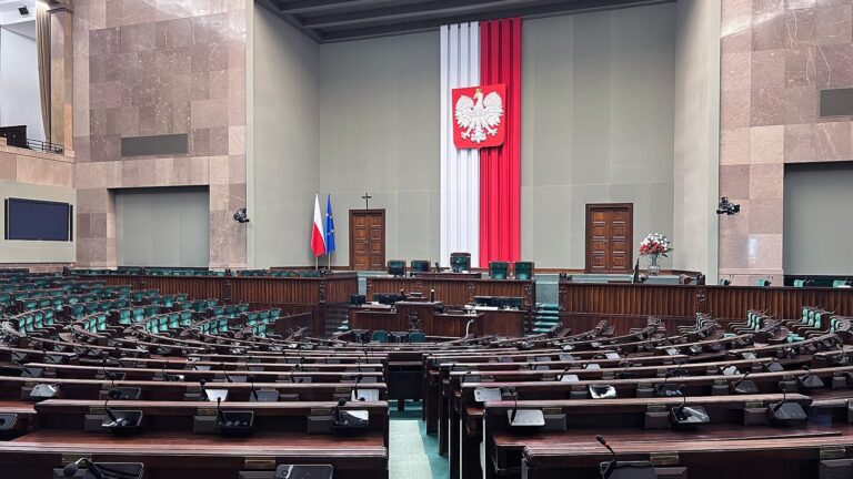 Sala posiedzeń Sejmu RP z pustymi ławami poselskimi i godłem Polski na ścianie