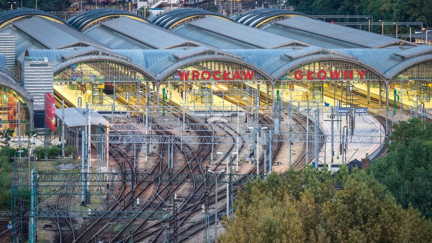 Widok z góry na perony i tory Dworca Głównego we Wrocławiu, z napisem „Wrocław Główny” na szklanych wiatach.